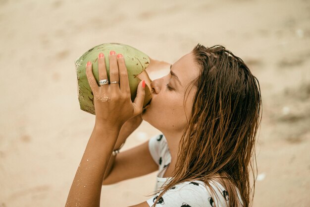 молодая женщина пьет тропический кокос на пляже