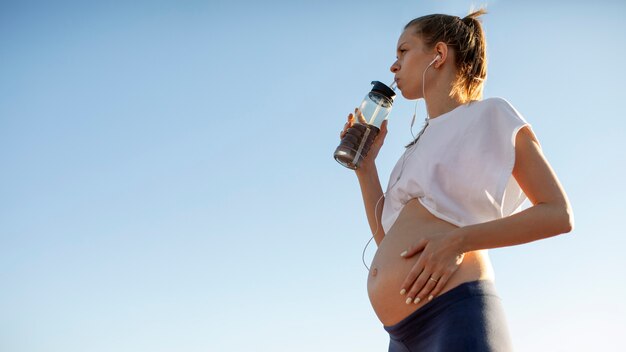 Молодая женщина пьет воду после тренировки во время беременности с копией пространства