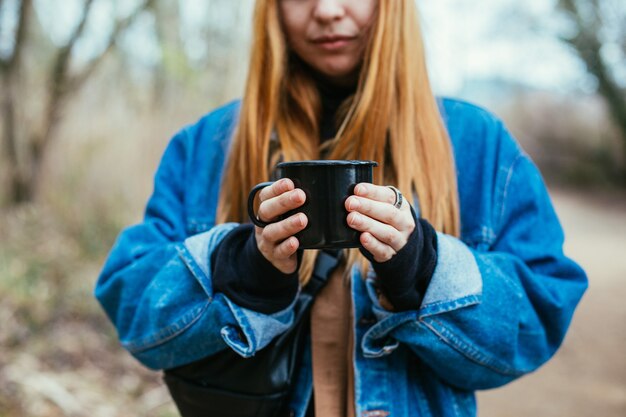 若い女性は湖岸でコーヒーカップを飲みます