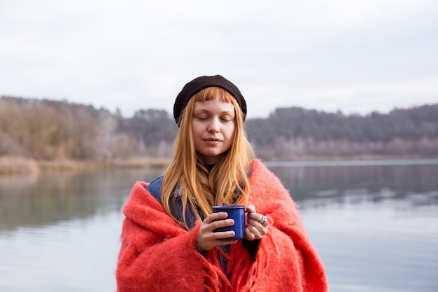若い女性は湖岸でコーヒーカップを飲みます