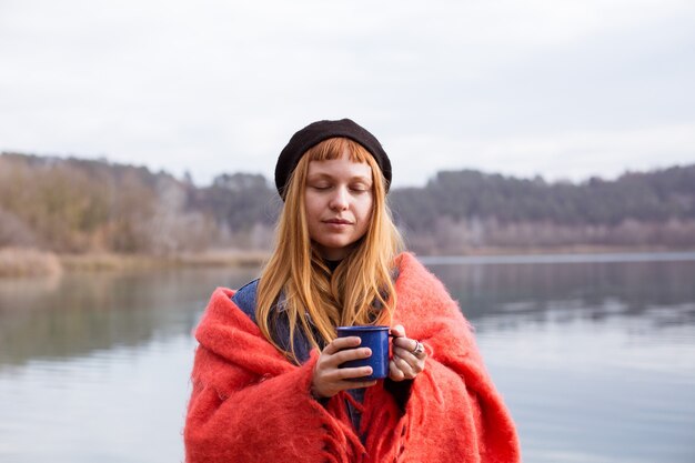 若い女性は湖岸でコーヒーカップを飲みます