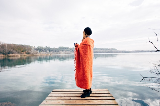 Young woman drinks coffee cup on lake shore