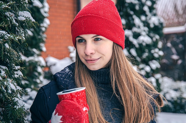 若い女性は冬に赤いサーマルカップから温かい飲み物を飲みます