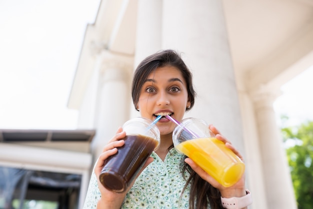 Young woman drinks two cocktails with ice in plastic cups with straw