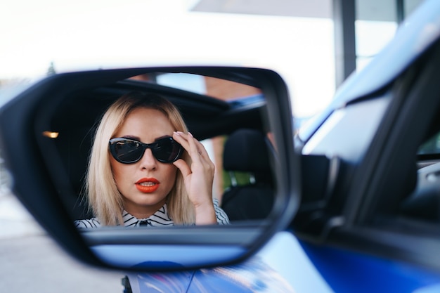 Young woman driver looking in car side view mirror, making sure line is free before making a turn.