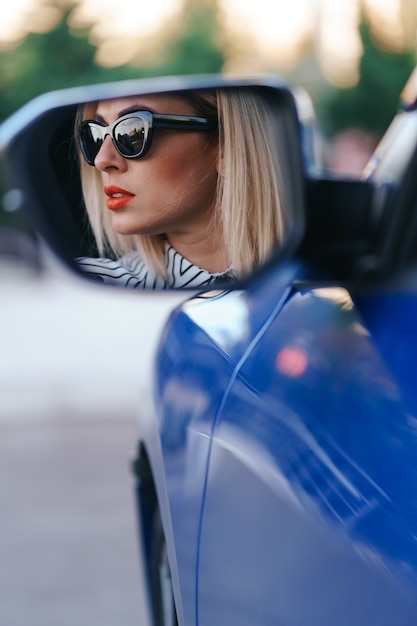 Молодая женщина-водитель смотрит в зеркало бокового вида автомобиля, перед поворотом проверяет, свободна ли линия.