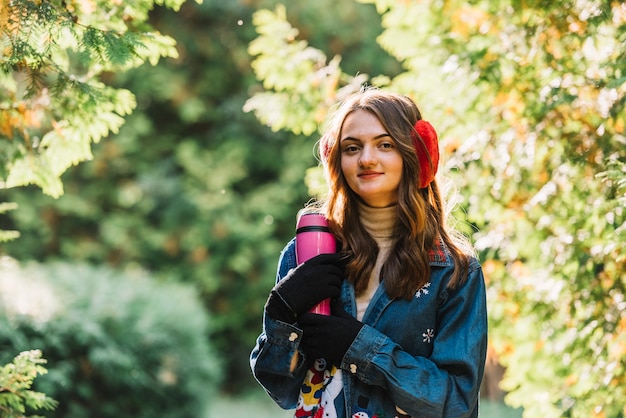 Foto gratuita giovane donna in cuffia che tiene thermos nel parco