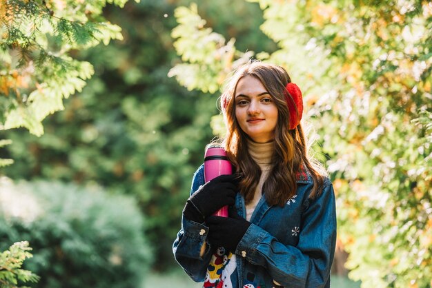 Young woman in earmuffs holding thermos in park