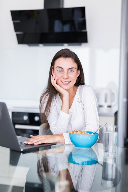 Young woman eat salad working on laptop in the kitchen