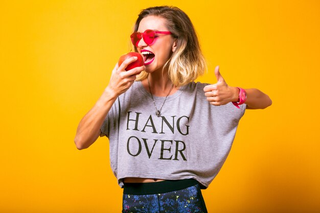 Young woman eating apple and showing ok gesture