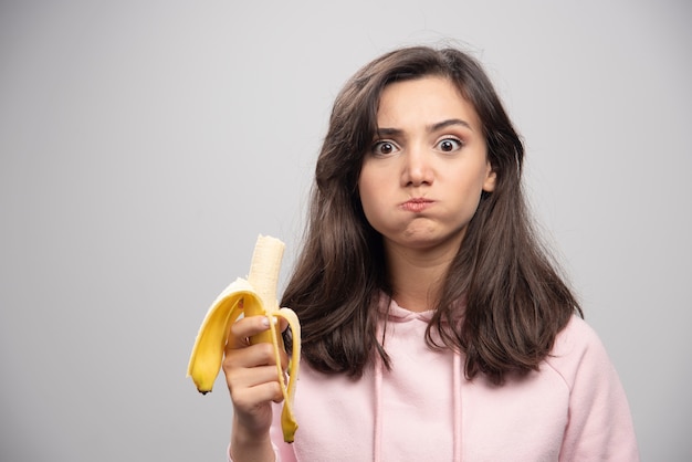 灰色の壁にバナナを食べる若い女性。