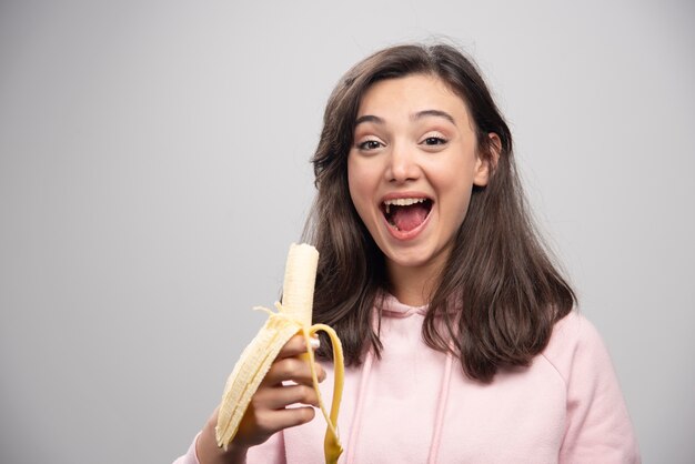 灰色の壁にバナナを食べる若い女性。