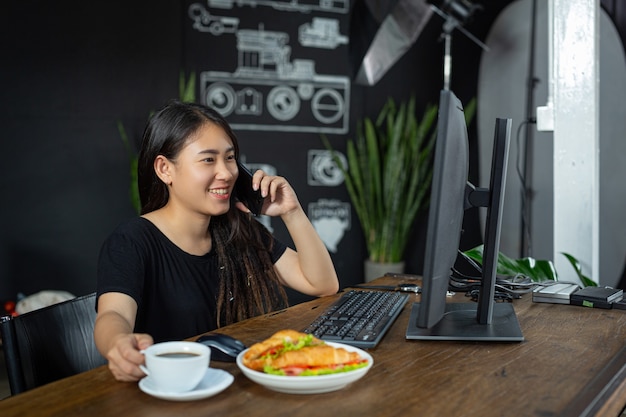 Young woman eating croissant sandwiches in office room