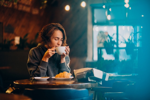 カフェでクロワッサンを食べる若い女性