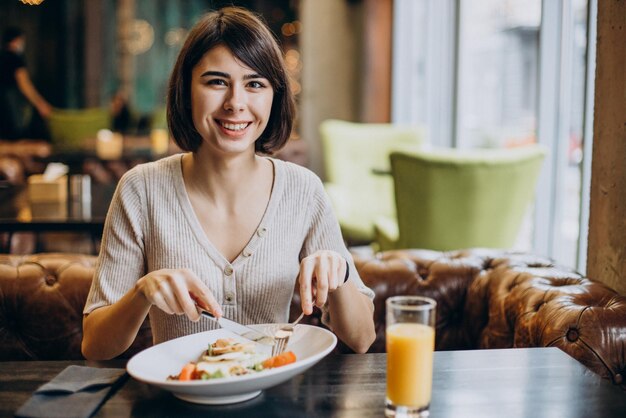 Молодая женщина есть здоровый завтрак с соком в кафе
