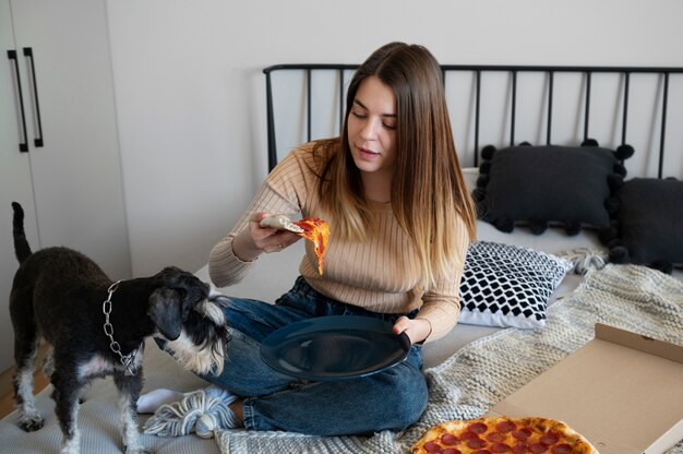 Молодая женщина ест пиццу на кровати
