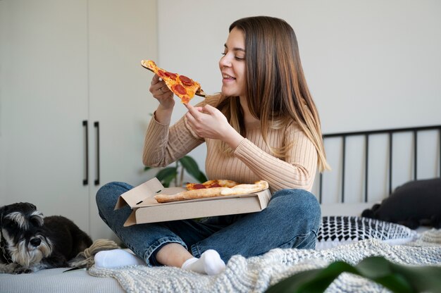 Young woman eating pizza on bed