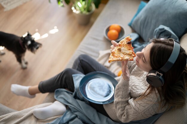 Young woman eating pizza and listening to music