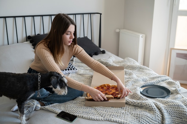 Молодая женщина ест пиццу на кровати