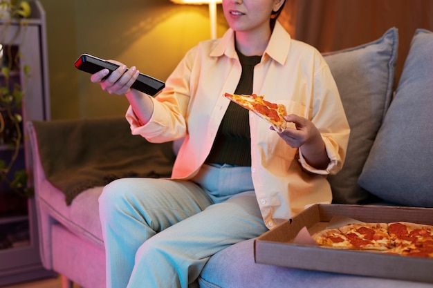 Молодая женщина ест пиццу и смотрит телевизор
