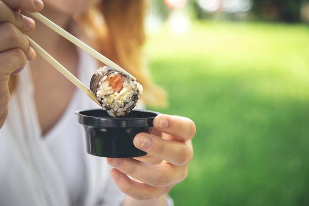 Молодая женщина ест суши на природе маки ролл крупным планом