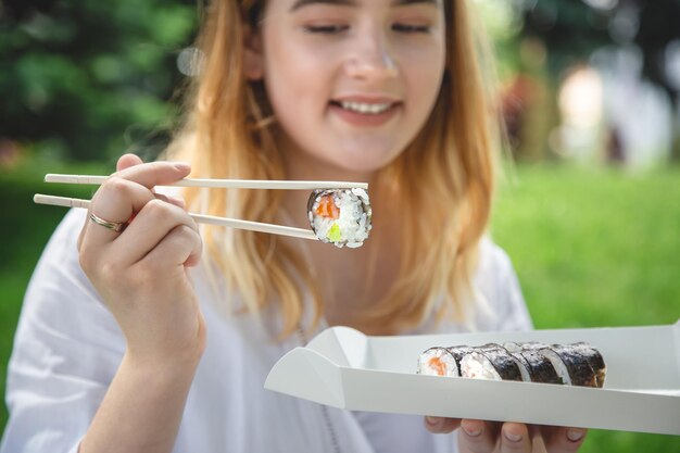 A young woman eating sushi in nature maki roll closeup