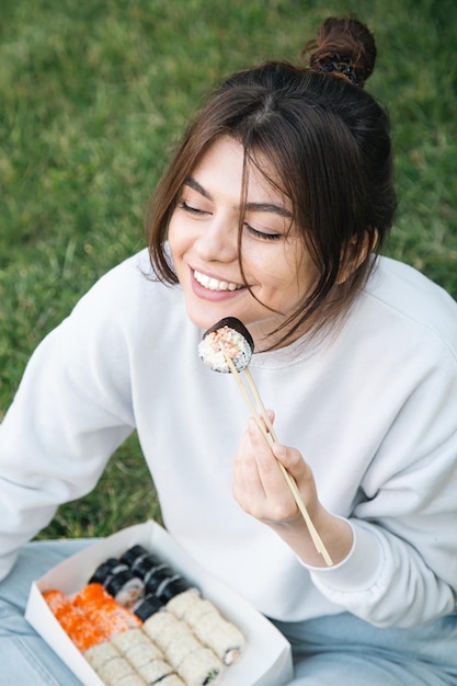 自然の中で公園のピクニックで寿司を食べる若い女性