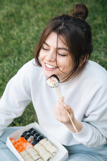 Молодая женщина ест суши на пикнике в парке на природе