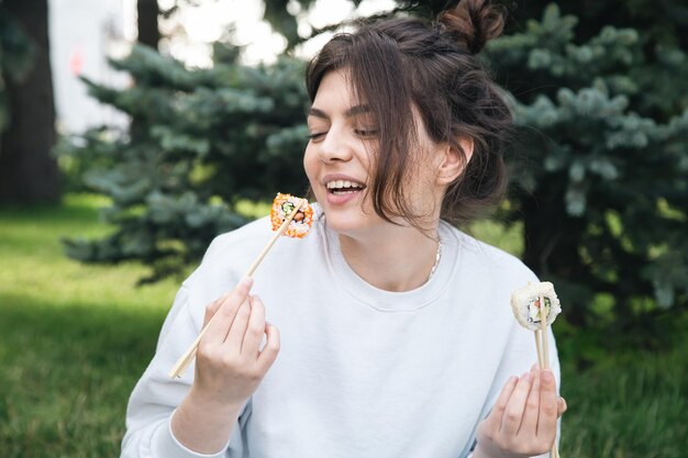 自然の中で公園のピクニックで寿司を食べる若い女性