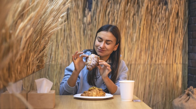 若い女性がカフェでコーヒーとクロワッサンを食べる