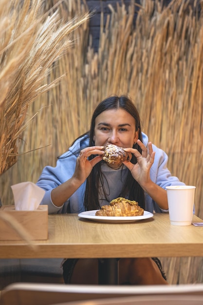 Free photo a young woman eats croissants with coffee in a cafe