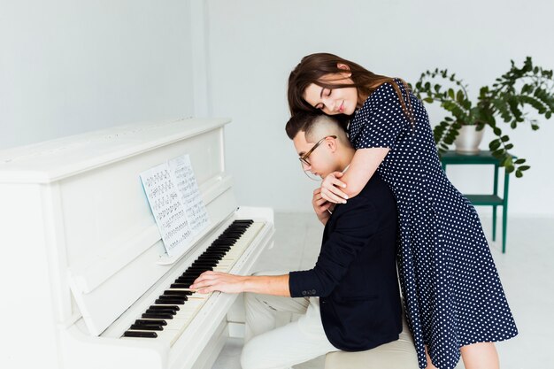 Young woman embracing her boyfriend from behind playing piano