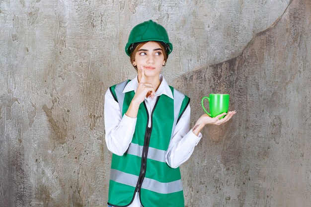 緑のベストを着て、コーヒーカップを保持している若い女性エンジニア