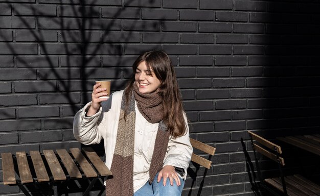 コーヒーショップの外観のレンガの壁に飲み物を楽しんでいる若い女性
