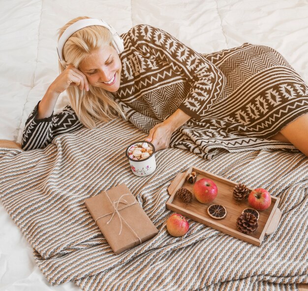 Free photo young woman enjoying music and hot beverage on bed