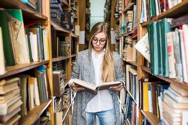 Young woman enjoying reading between bookshelves