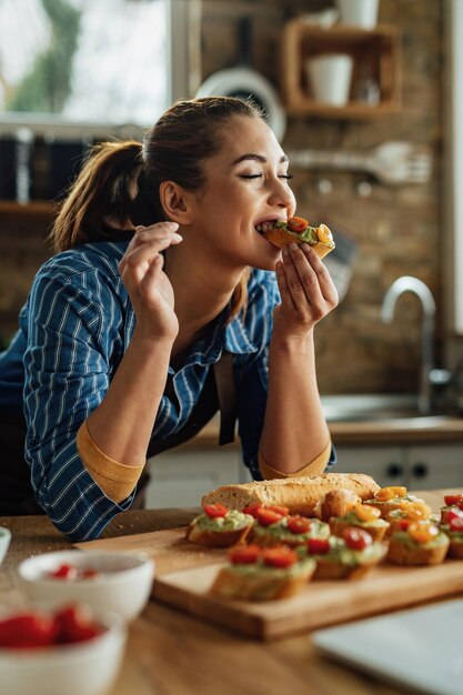 Young woman enjoying in taste on healthy bruschetta with her eyes closed in the kitchen