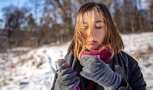 A young woman enjoys a hot drink from a thermos on a walk in winter