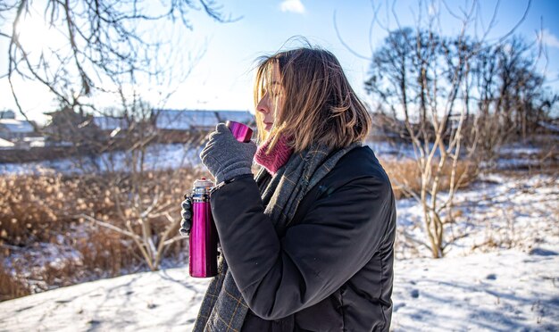 A young woman enjoys a hot drink from a thermos on a walk in winter