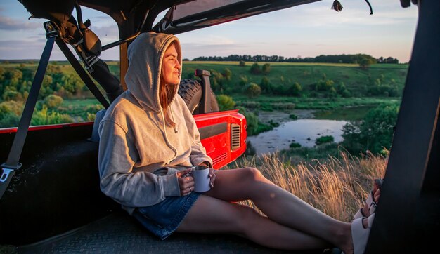 A young woman enjoys the sunset while sitting in the trunk of an suv