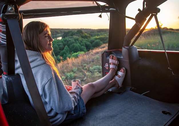 A young woman enjoys the sunset while sitting in the trunk of an suv