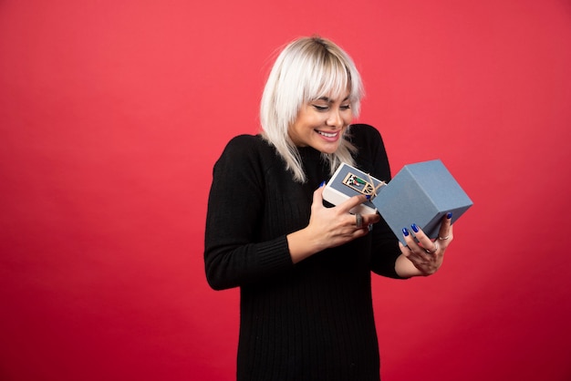 Young woman excited about a present on a red wall. 