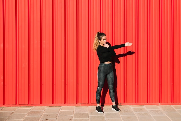 Young woman exercising near red wall