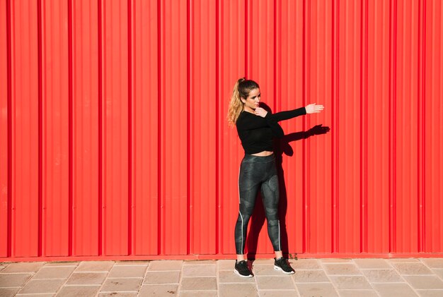 Young woman exercising near red wall