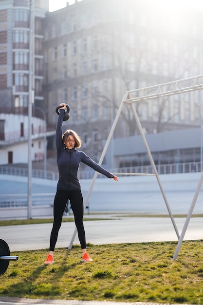 Foto gratuita giovane donna che si esercita con un kettlebell fuori allo stadio