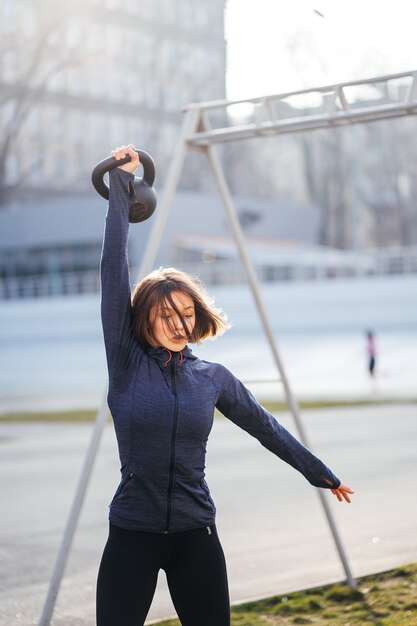 Young woman exercising with a kettlebell outside at stadium