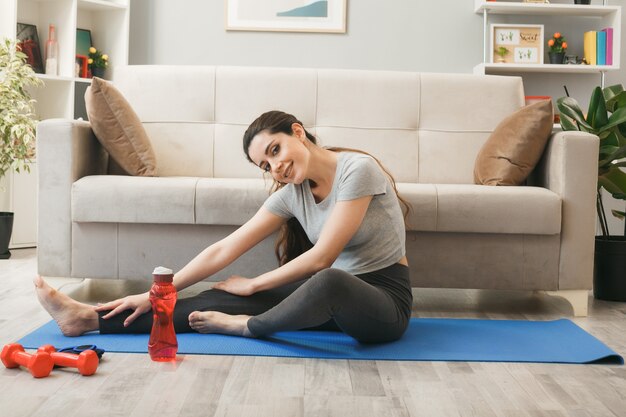 Молодая женщина упражнениями на коврике для йоги перед диваном в гостиной