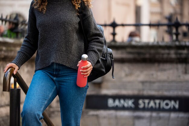 Молодая женщина выходит из метро и держит бутылку с водой в городе