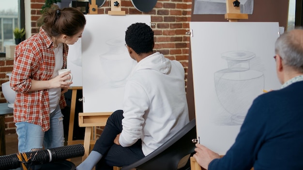 Бесплатное фото Молодая женщина объясняет художественный урок студенту в художественном классе. творческий человек использует карандаш и холст с мольбертом, рисует шедевр вазы, чтобы освоить новые навыки в мастерской с учителем.