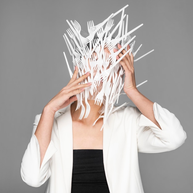 Young woman face being covered in white plastic forks
